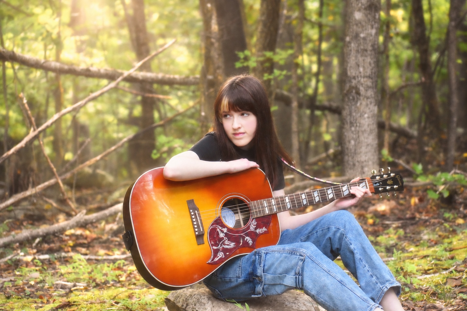 Josette Seraphine sitting in the woods with her sunburst acoustic guitar